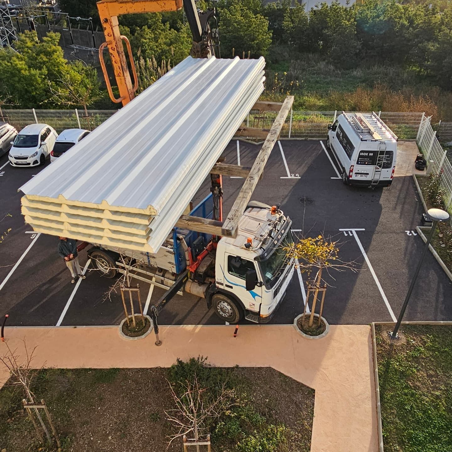 Grue soulevant des panneaux de construction d'un camion dans un parking.