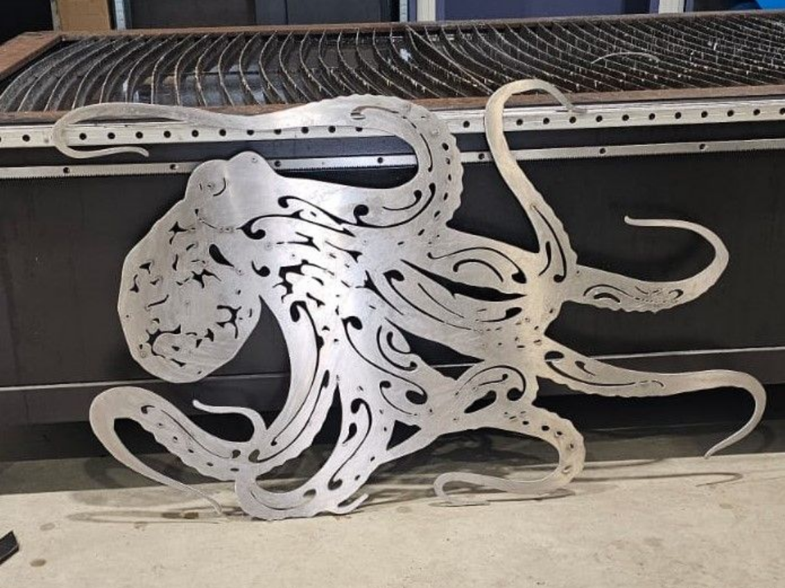 Sculpture de pieuvre en métal avec un design découpé complexe, reposant sur une surface métallique.