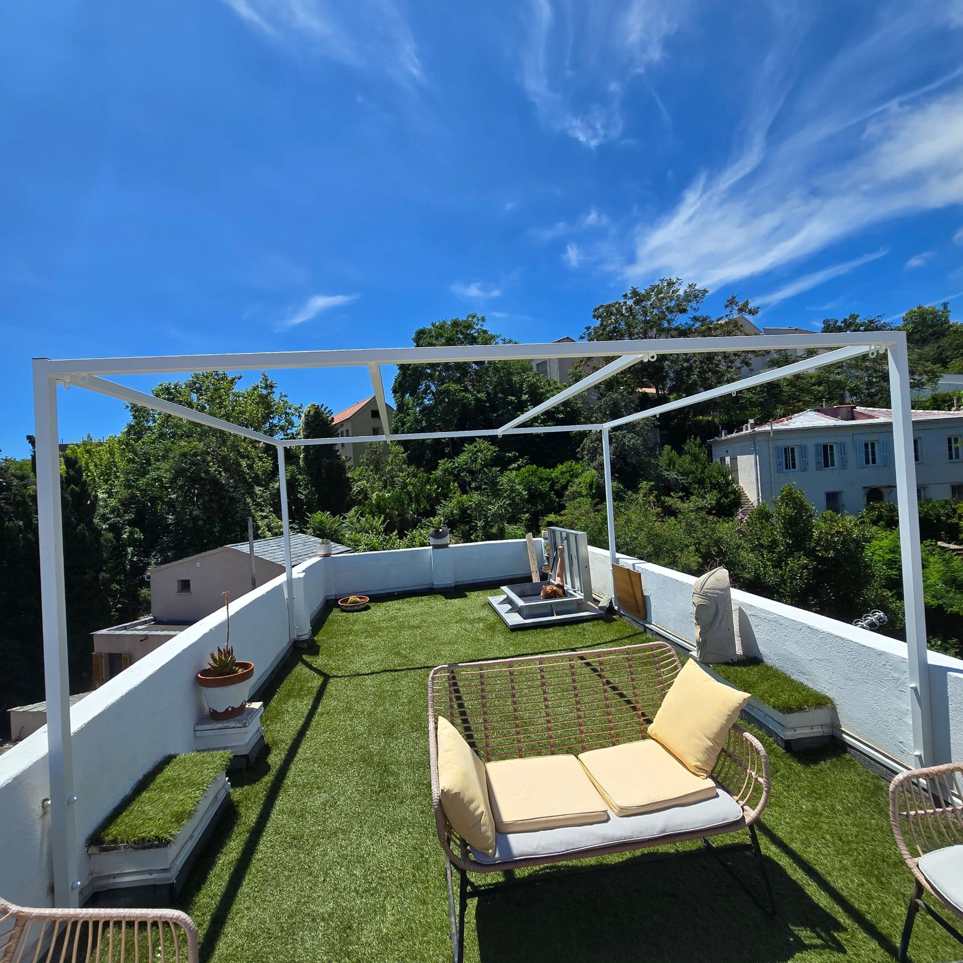 Pergola en métal noir sur un bâtiment blanc contre un ciel bleu clair.