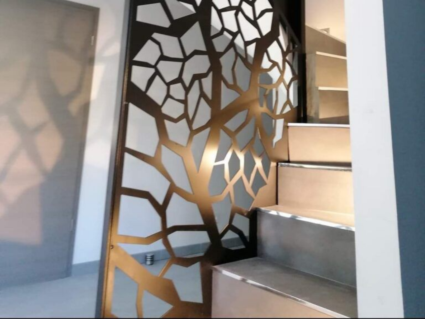 Paravent décoratif en métal avec motif de branche d'arbre, à côté des escaliers.