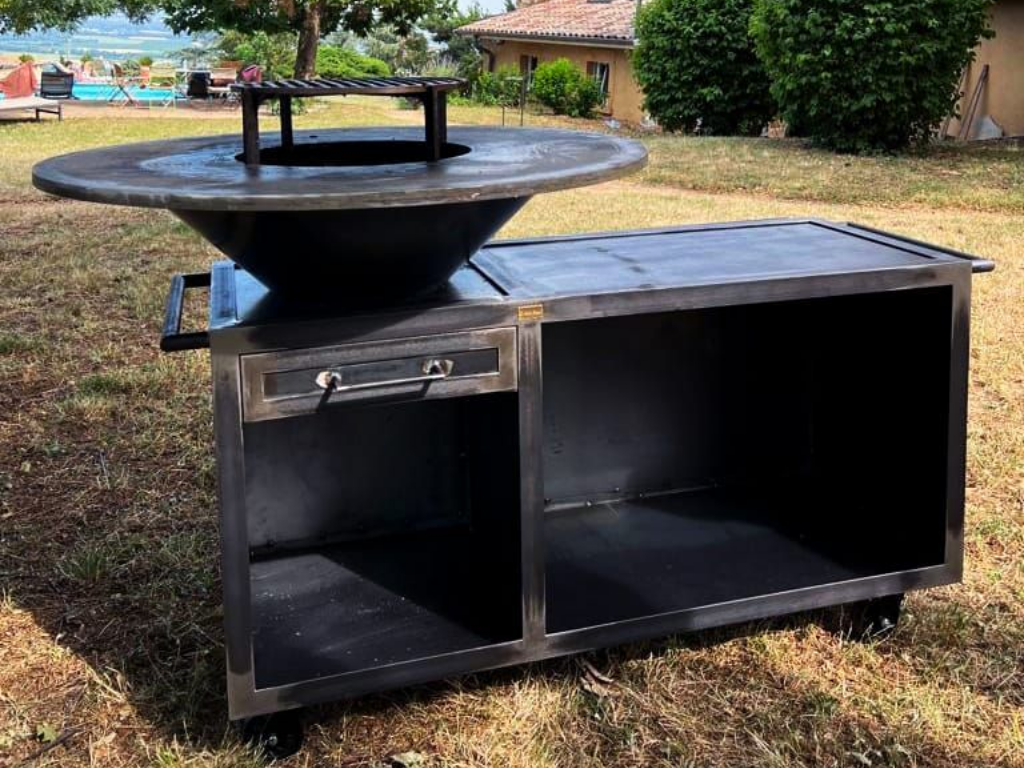 Braséro extérieur en métal avec surface de cuisson et rangement, située dans une cour herbeuse.