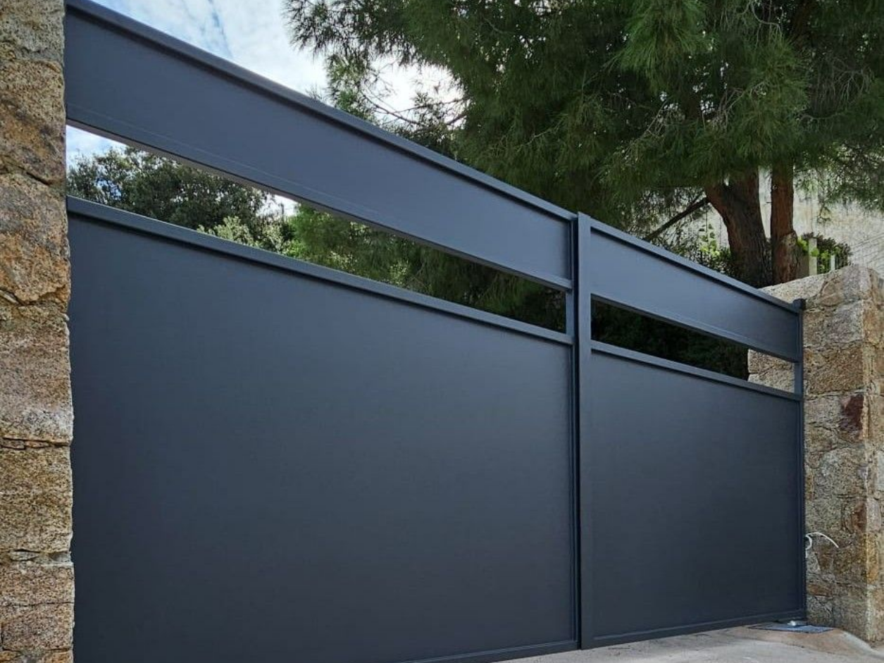 Portail d'allée en métal gris à ouvertures horizontales, placé entre des colonnes en pierre.