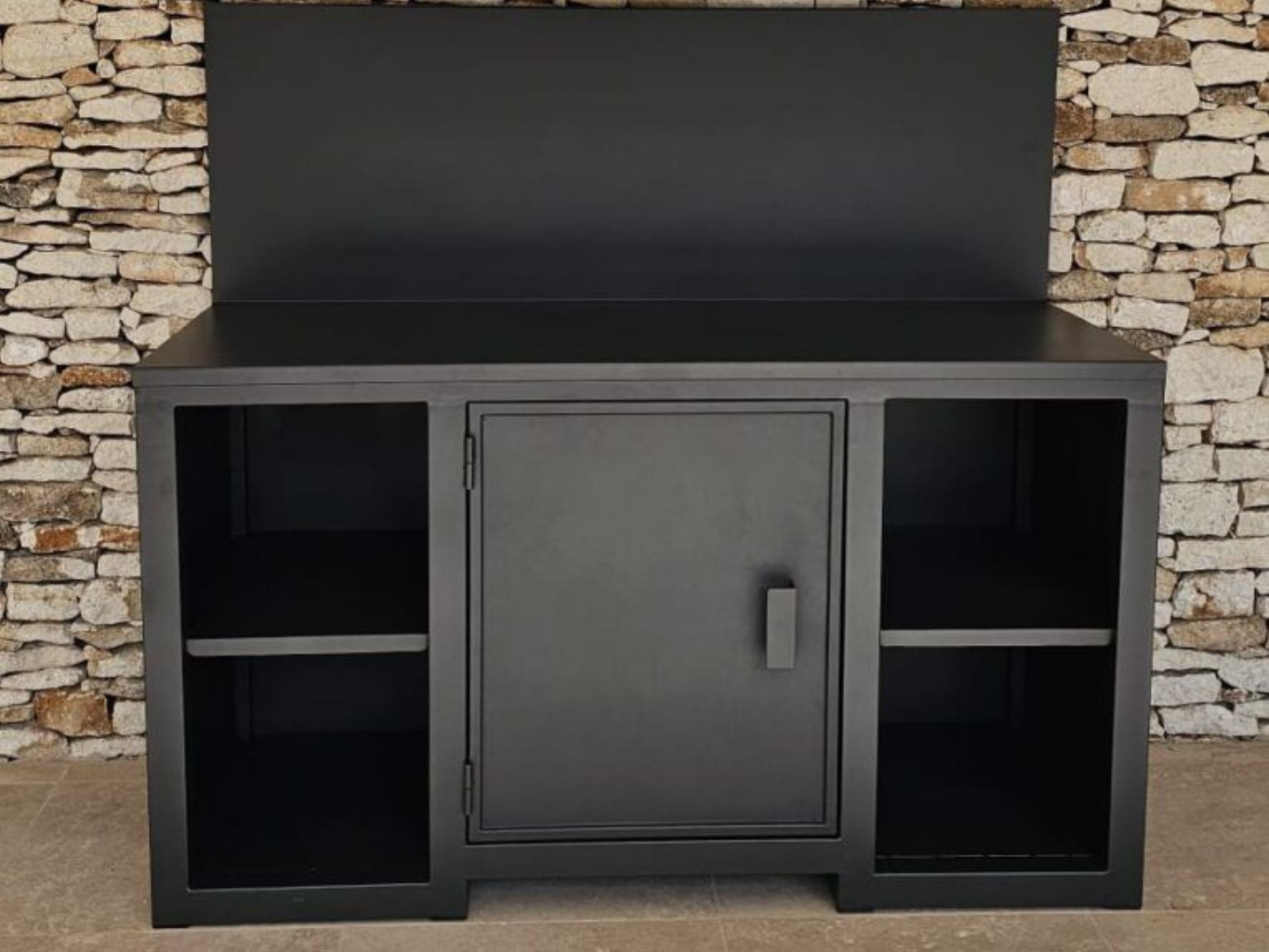 Poste de travail en métal noir avec porte d'armoire, étagères et dosseret, adossé à un mur en pierre.