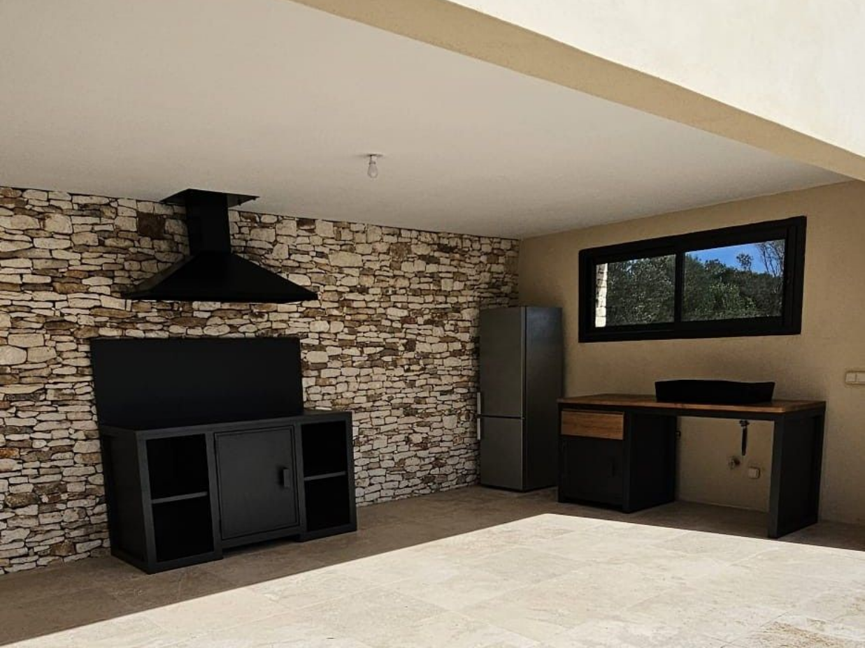 Cuisine extérieure avec mur d'accent en pierre, armoires noires, hotte de cuisinière et réfrigérateur.