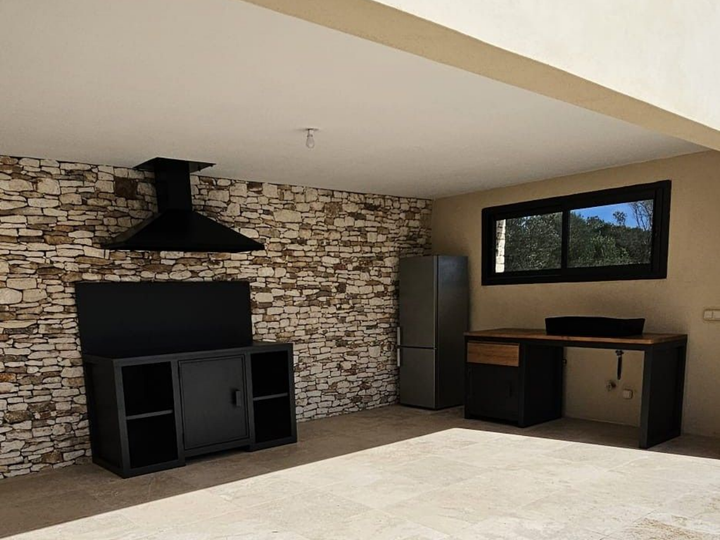 Cuisine extérieure avec mur d'accent en pierre, armoires noires, hotte de cuisinière et réfrigérateur.