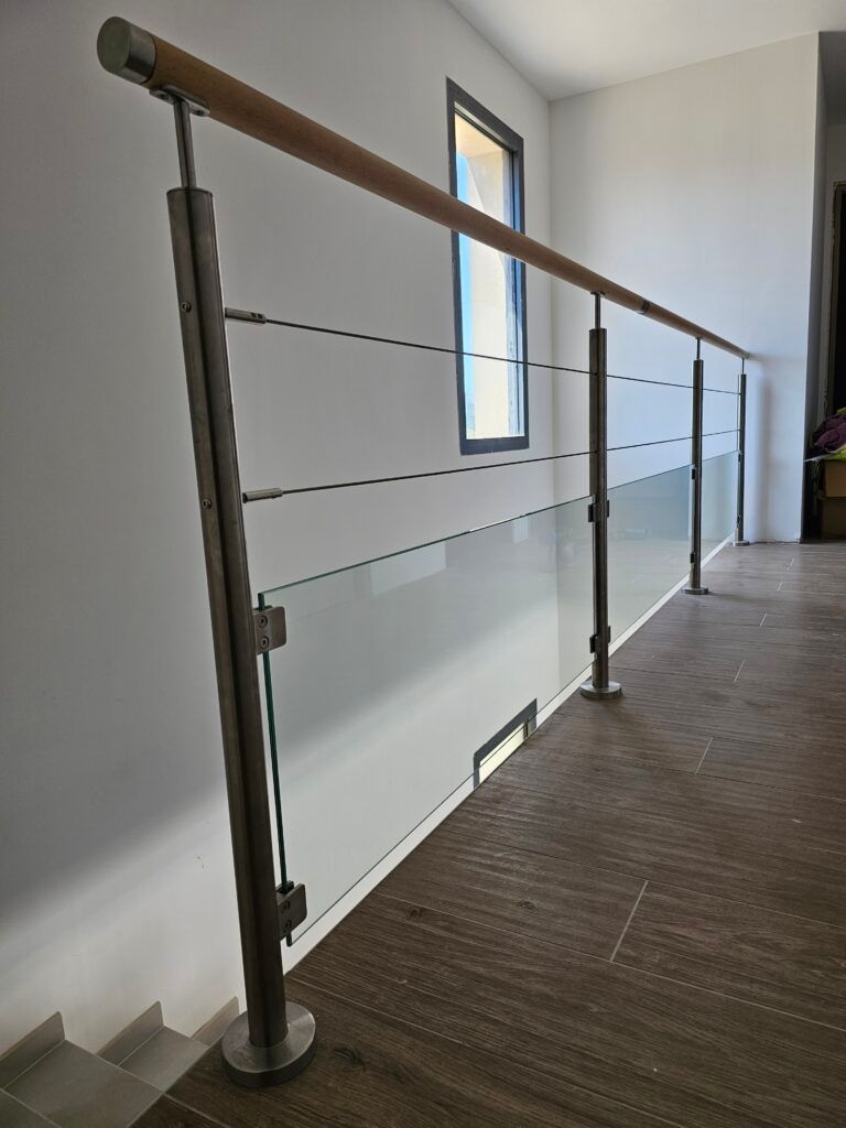 Un intérieur moderne avec rampe en acier inoxydable et verre. Main courante en bois clair. Moquette marron.