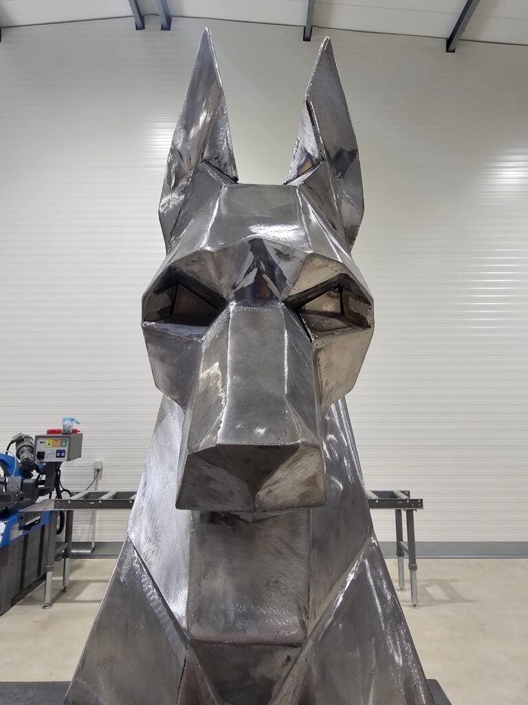 Sculpture géométrique en métal représentant un chien assis. L'œuvre se situe dans un décor industriel.