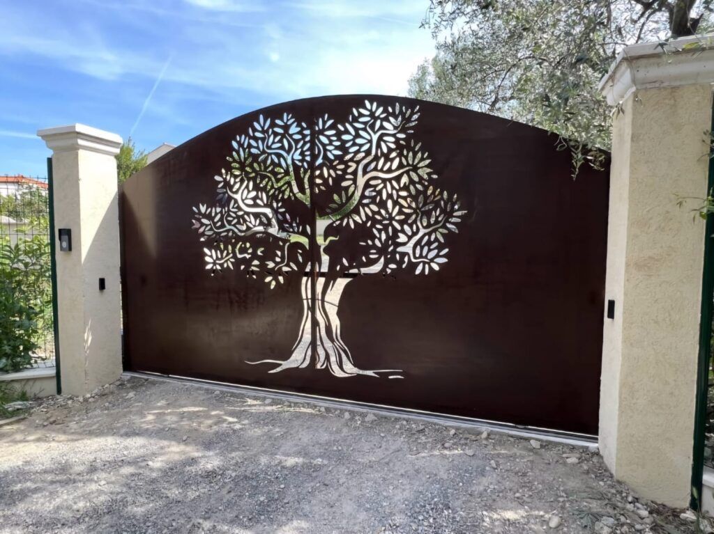 Portail en métal marron foncé avec un motif d'arbre découpé au laser entre des piliers de couleur crème.