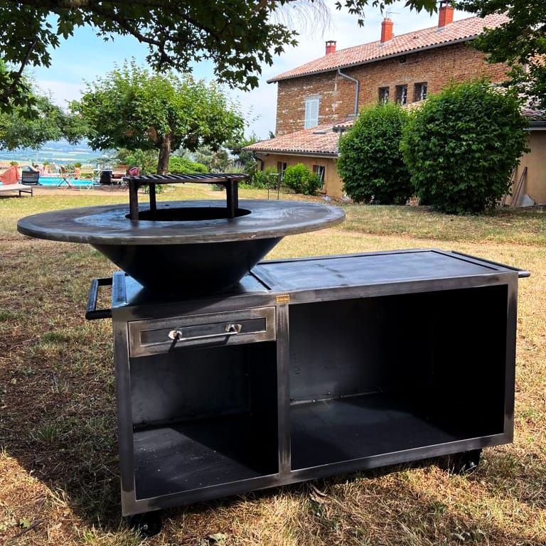 Braséro en métal et station de préparation avec surface de cuisson circulaire, tiroir et étagères ouvertes.