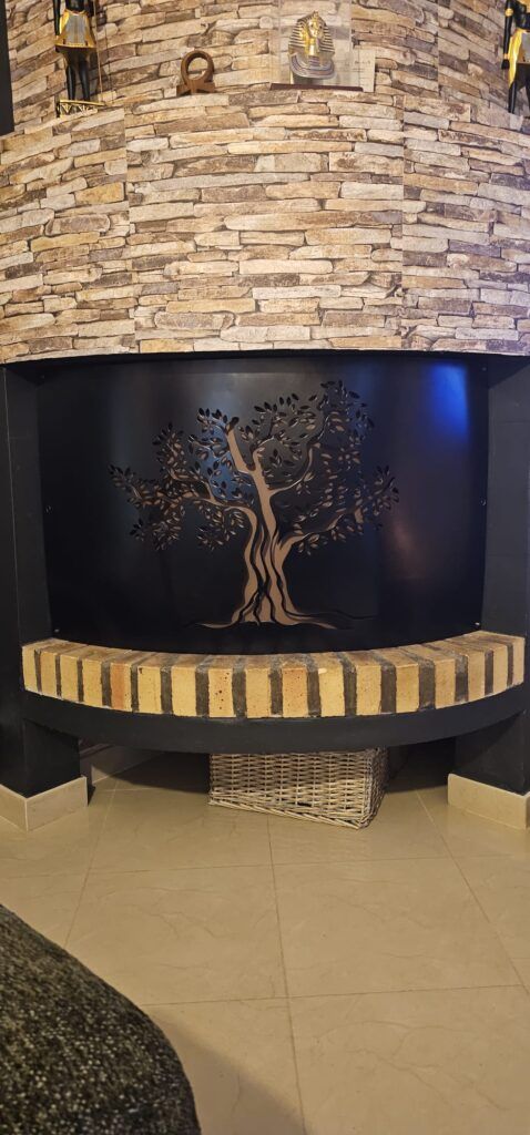 Cheminée avec façade en pierre, intérieur noir avec art d'arbre et un banc en brique.