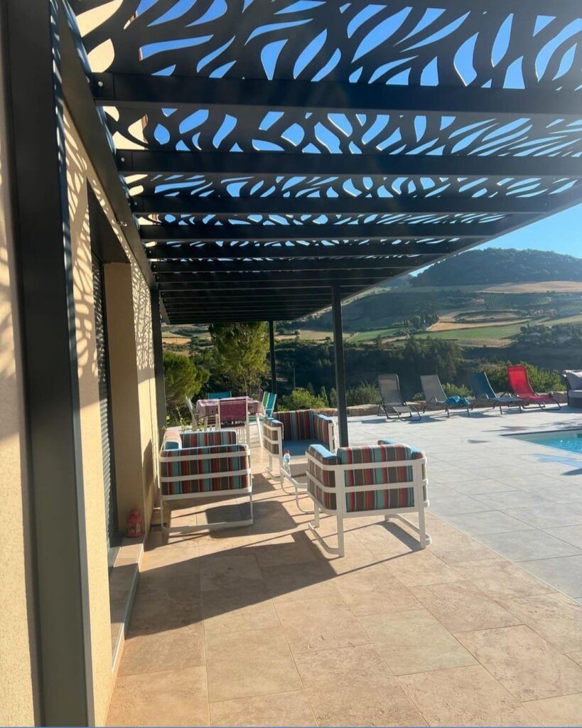 Patio avec ombrage décoratif surplombant la piscine et la vallée. Mobilier au premier plan.