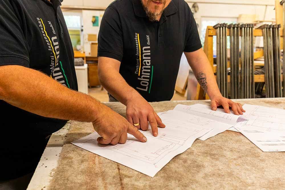 zwei Männer stehen an einem Tisch und schauen auf ein Blatt Papier mit der Aufschrift lohmann gmbh darauf