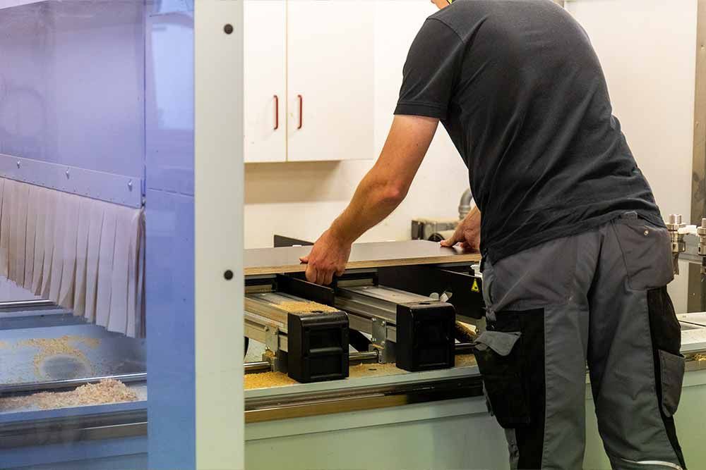 ein Mann steht neben einer Maschine und arbeitet an einem Stück Holz