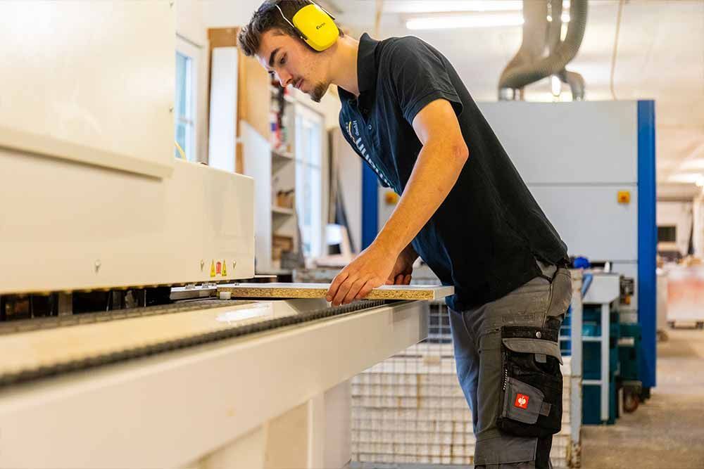 Ein Mann trägt Kopfhörer und arbeitet an einer Maschine in einer Fabrik .