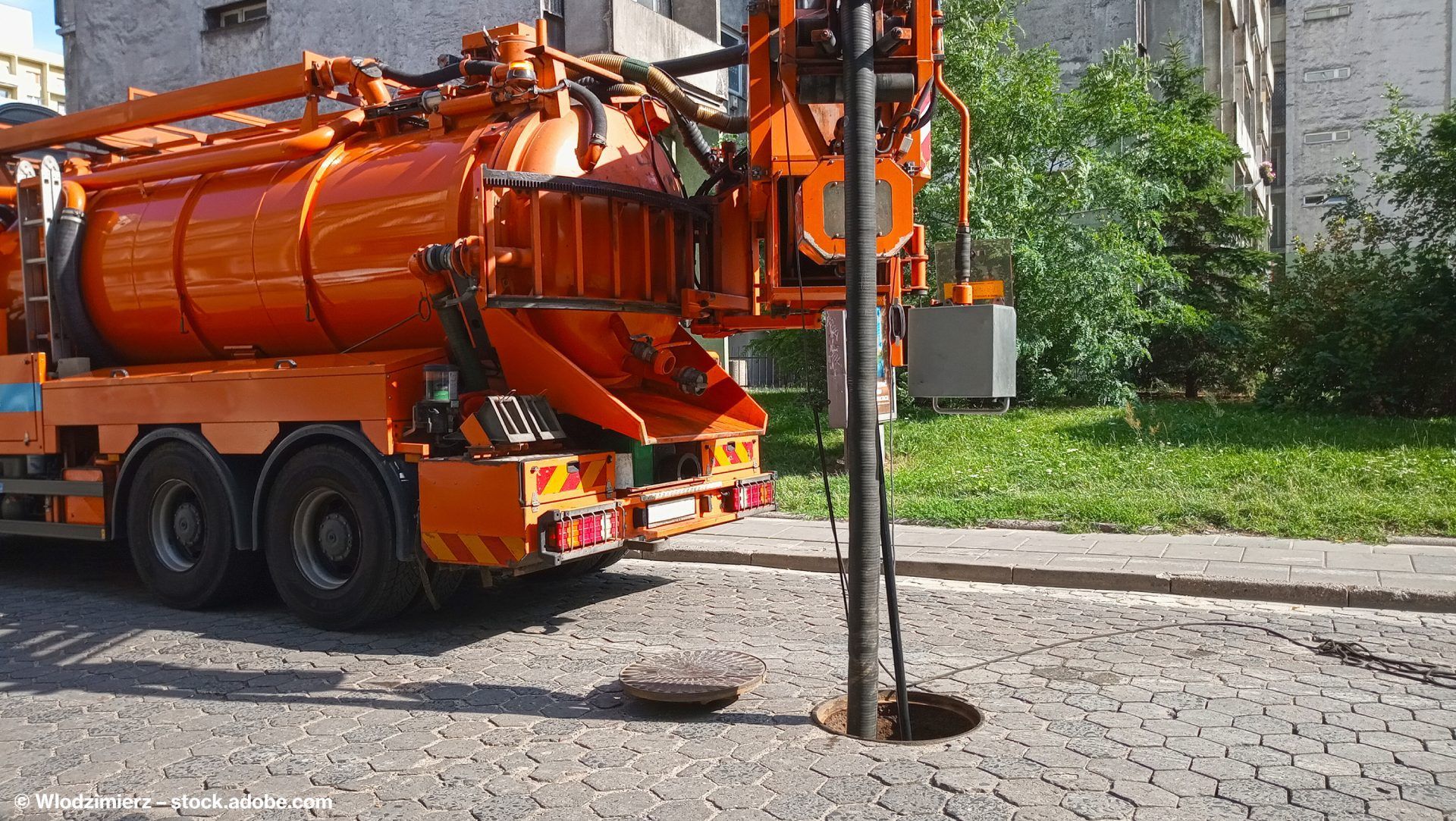Durchführung einer Rohrreinigung mithilfe eines großen orangenen Fahrzeugs auf einer Straße