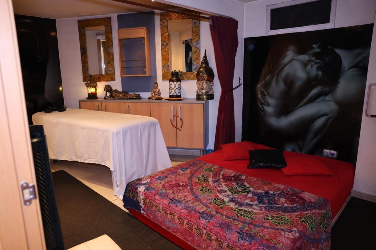 Dormitorio con una cama cubierta con una manta estampada roja, sábanas blancas y un mural oscuro en la pared sobre el cabecero.