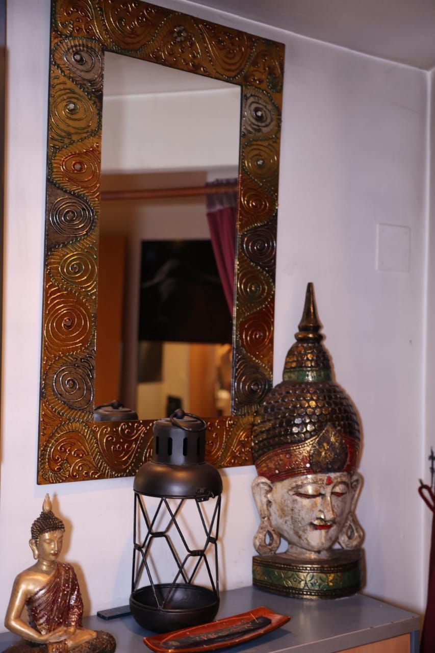 Estatua decorativa de Buda y farol en un estante junto a un espejo con marco dorado estampado.