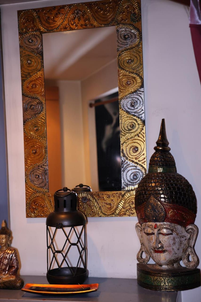 Espejo decorativo con marco ornamentado sobre un estante que sostiene una linterna, una estatua de Buda y un candelabro.