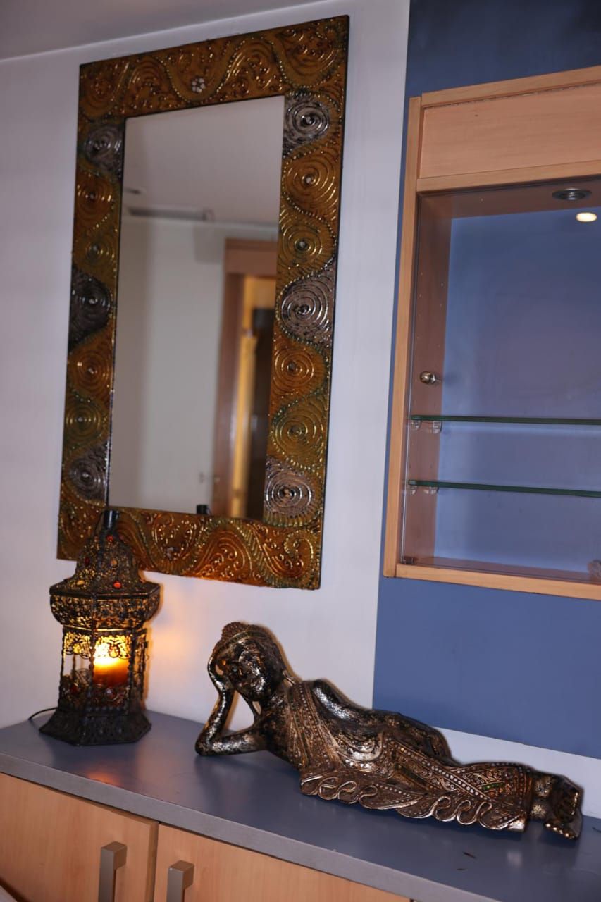 Espejo decorativo, farol y escultura reclinada sobre un estante junto a una ventana.