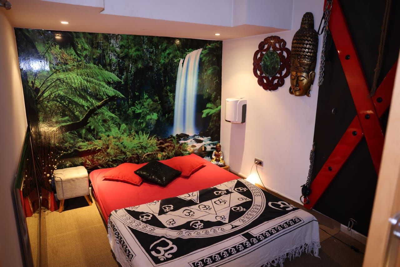 Dormitorio con temática tropical, con colcha roja, mural de cascada en la pared y decoración de bambú.