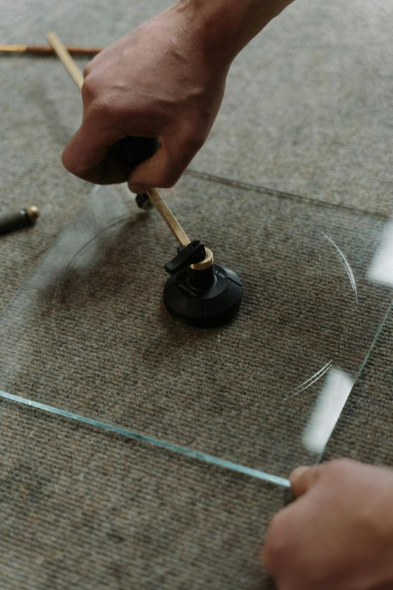 Gros plan sur la découpe d’une plaque de verre à l’aide d’un coupe-verre à ventouse. Une main guide l’outil pour tracer une forme circulaire sur le verre transparent posé sur une surface de travail.