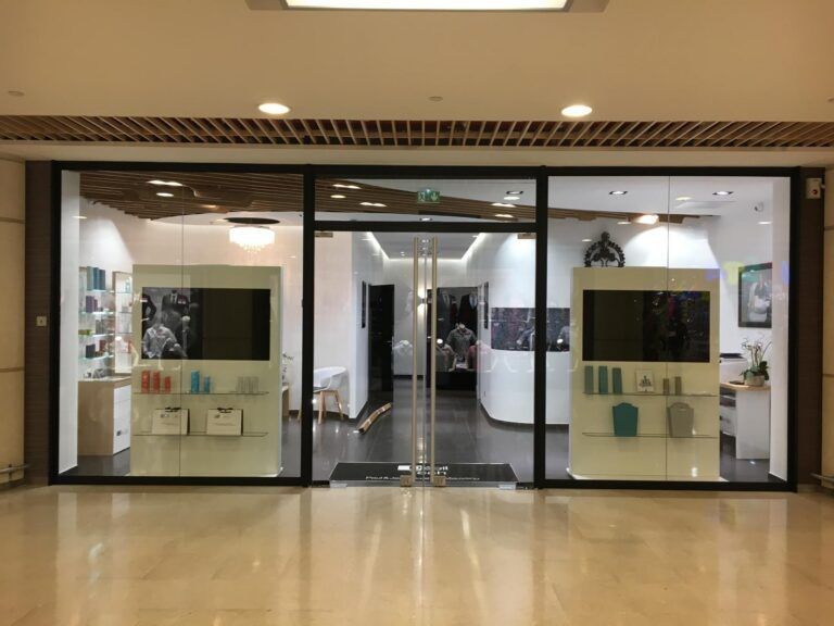 Boutique fermée avec des portes vitrées et des vitrines dans une galerie marchande lumineuse.