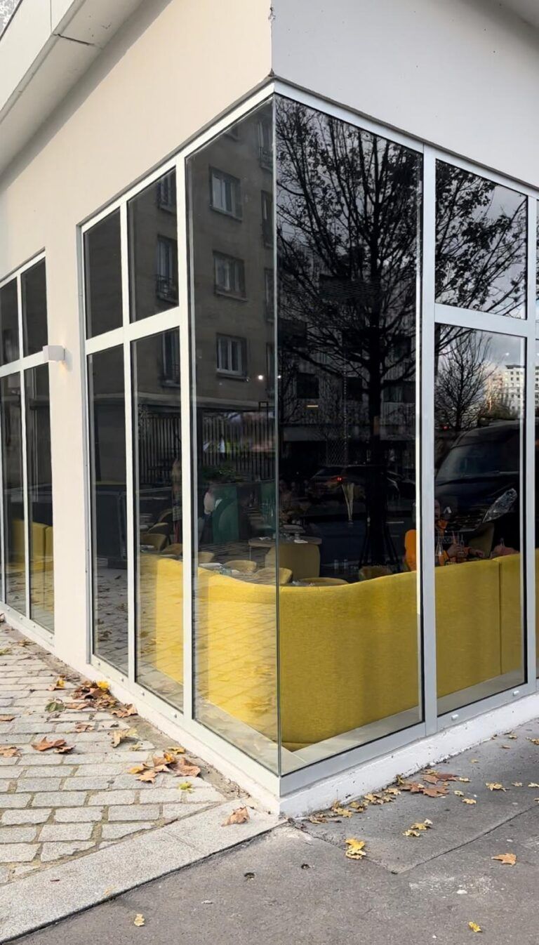 Vitrine d’angle en verre avec des panneaux jaunes en partie basse, au bord d’un trottoir.