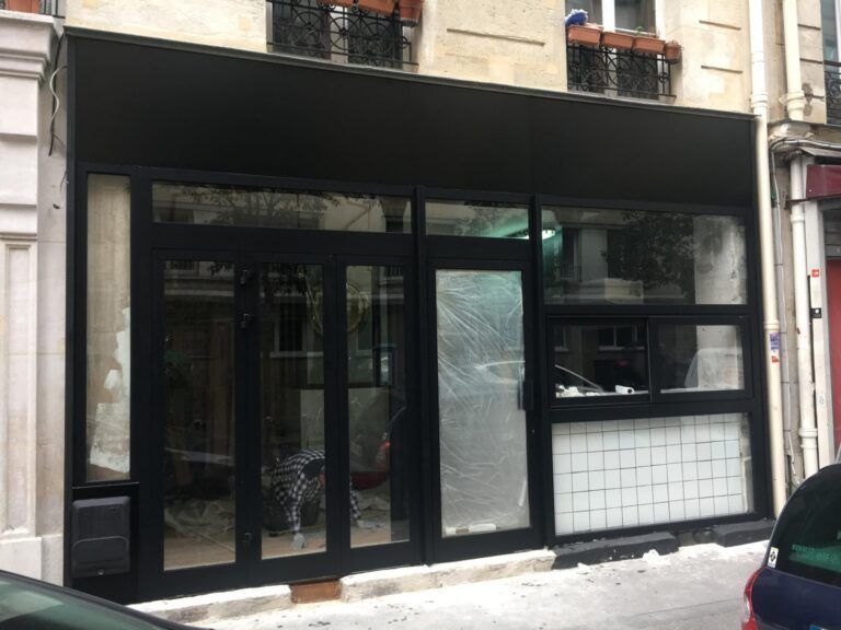 Façade noire avec de grandes baies vitrées et un soubassement carrelé, dans une rue en ville.