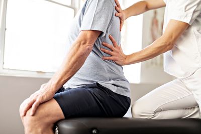 Physiotherapeut stützt den Rücken eines sitzenden Patienten während einer Behandlungssitzung