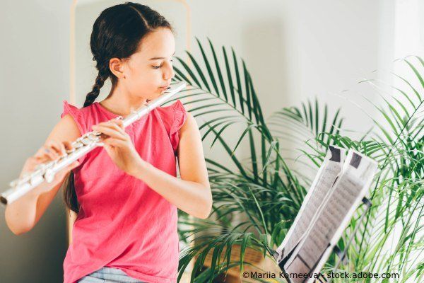 Mädchen spielt eine silberne Flöte und liest Noten, im Hintergrund eine Pflanze.