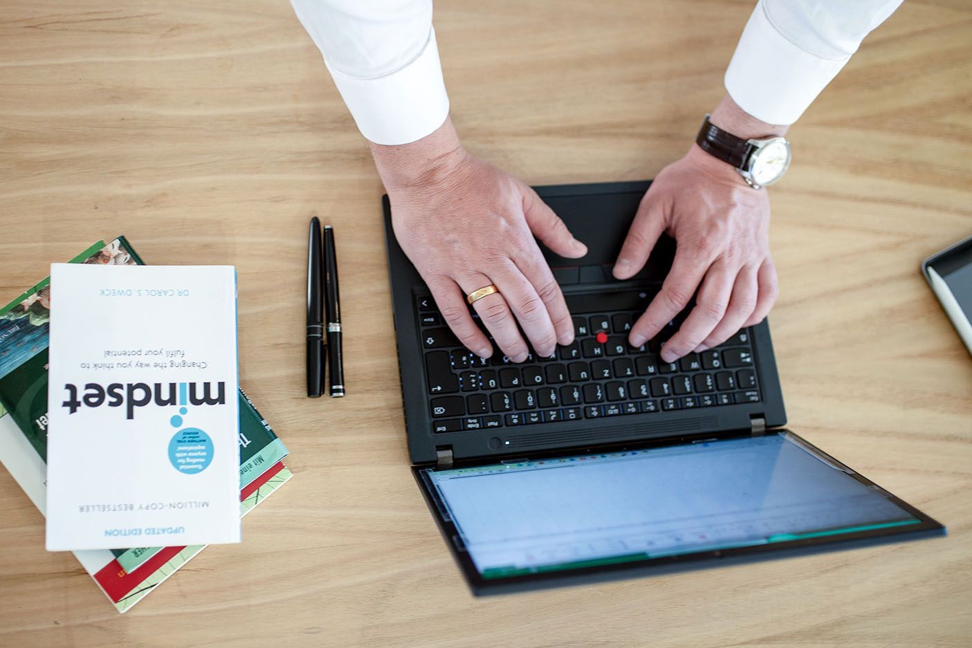 Ein Mann tippt auf einem Laptop neben einem Buch mit dem Titel „Mindset“.