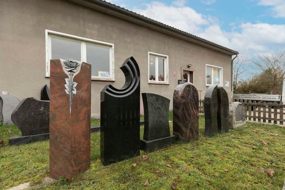 Vor einem Gebäude ist eine Reihe von Grabsteinen aufgestellt.