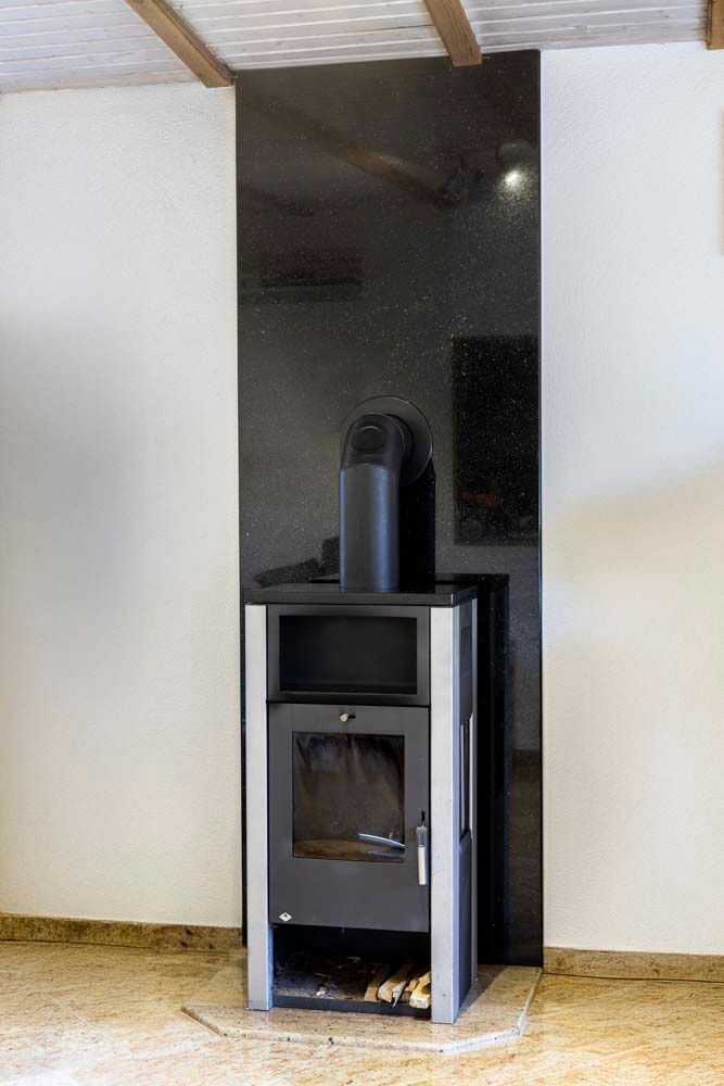 In einem Raum neben einer weißen Wand steht ein schwarzer Kamin.