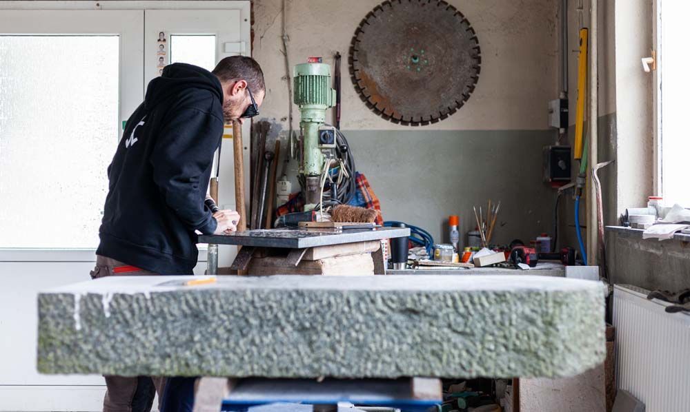 Ein Mann bearbeitet in einer Werkstatt ein großes Stück Stein.