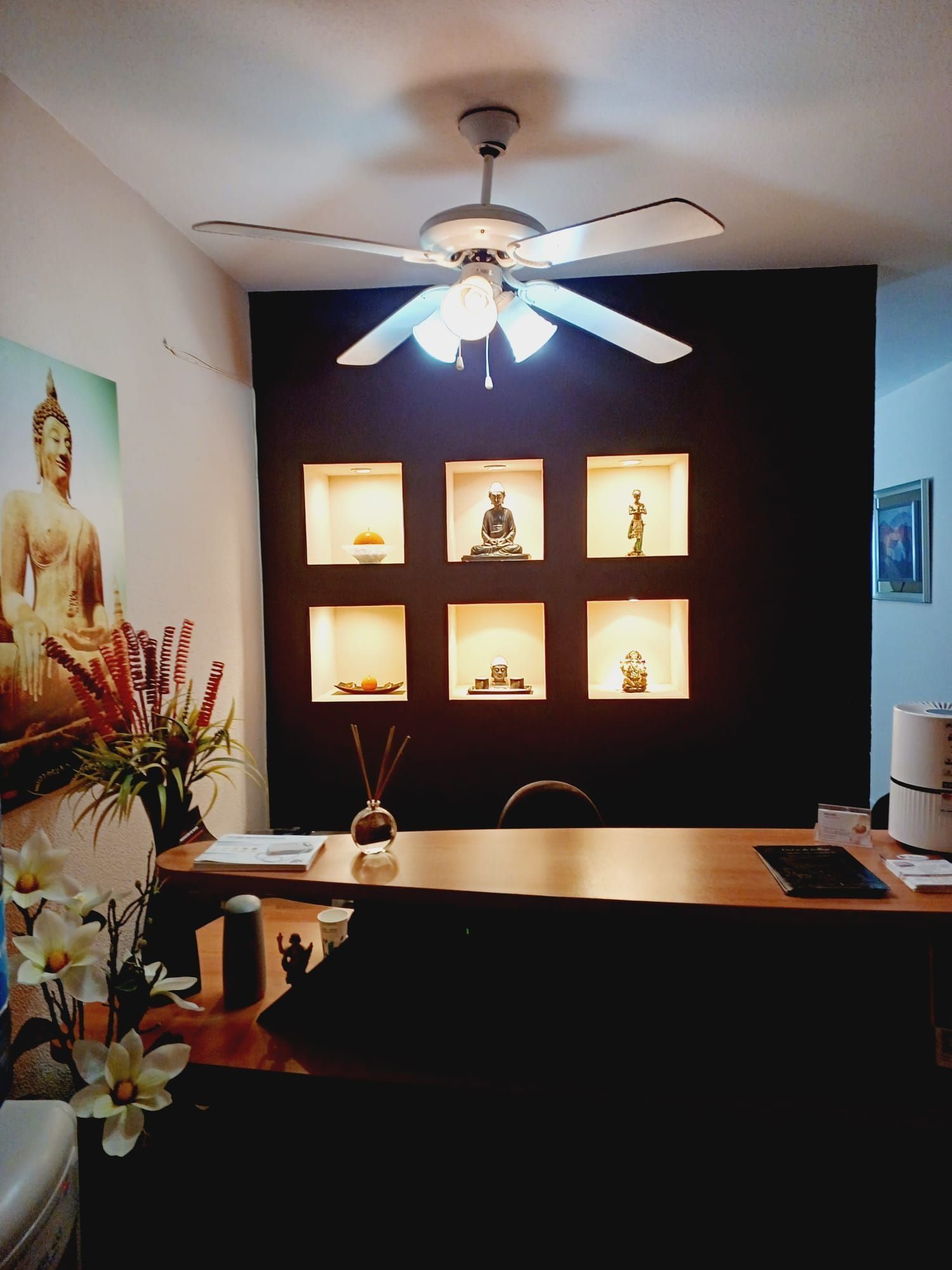 Área de recepción con arte de Buda, pared de acento oscuro con estantes de exhibición iluminados y un ventilador de techo.