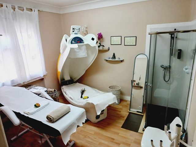 Sala de spa con mesa de masajes, cabina de sauna, ducha y espejo.