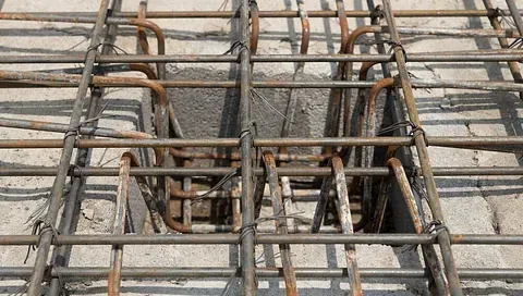Un agujero cuadrado en una losa de hormigón rodeado por una cuadrícula de armadura de acero para la construcción.