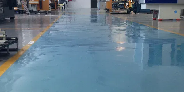 Un suelo industrial brillante de color azul claro con líneas amarillas que delimitan el pasillo, situado en el interior de un taller de fabricación.