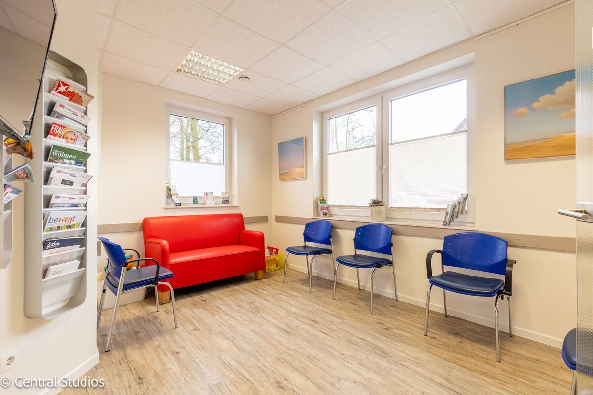Ein Wartezimmer mit einer roten Couch und blauen Stühlen.
