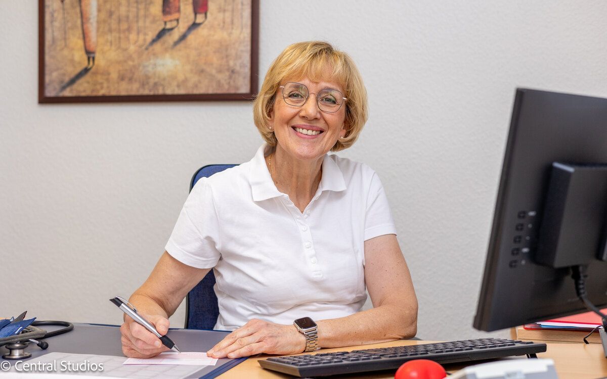 Fachärztin Marianne Lau sitzt an einem Schreibtisch vor einem Computer und lächelt.
