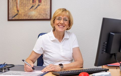 Fachärztin Marianne Lau sitzt an einem Schreibtisch vor einem Computer und lächelt.