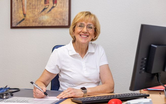 Fachärztin Marianne Lau sitzt an einem Schreibtisch vor einem Computer und lächelt.