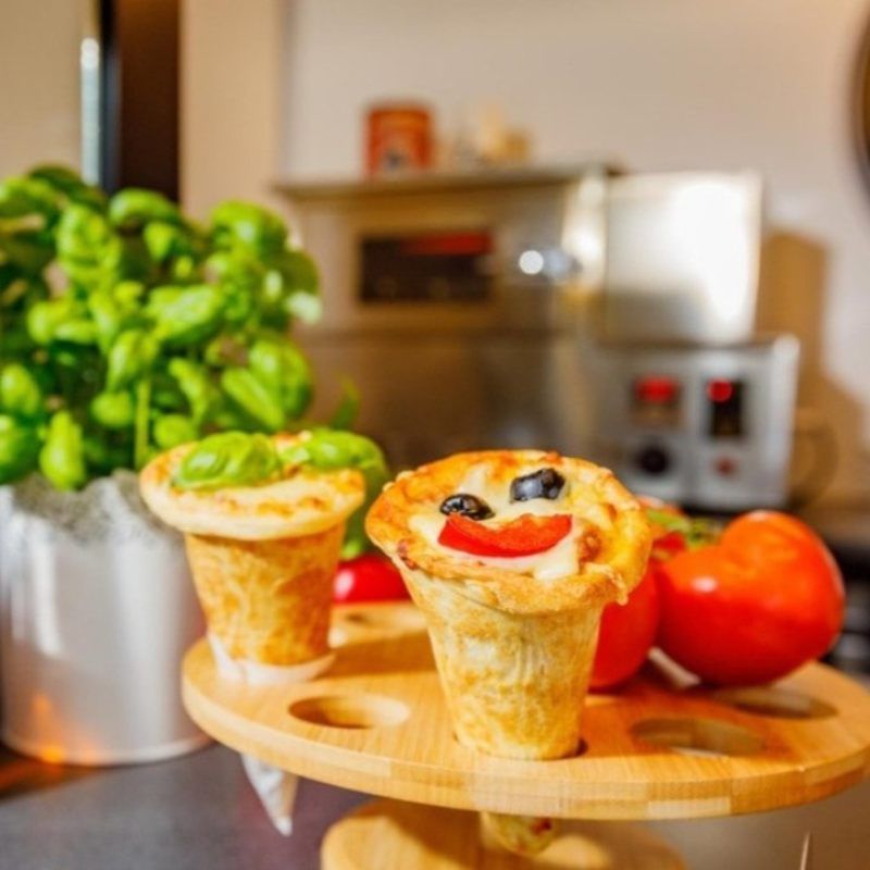 Desserthoorntjes met fruit erop, op een houten plank in een keuken, met een lachend gezichtje van fruit.