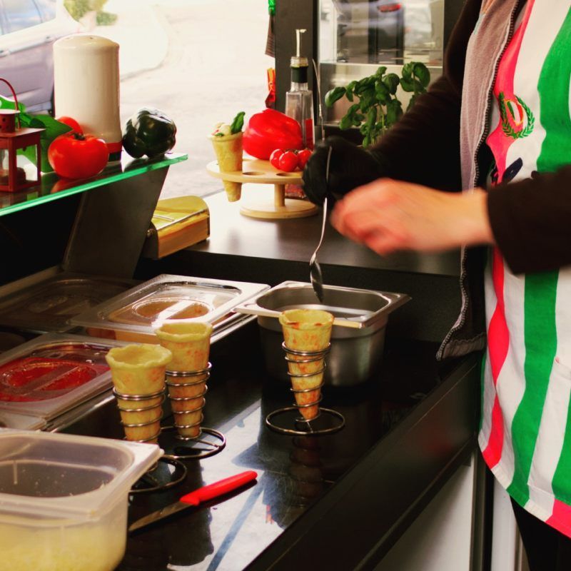 Iemand die eten klaarmaakt aan een aanrecht met bakjes ingrediënten en opgestapelde kopjes.