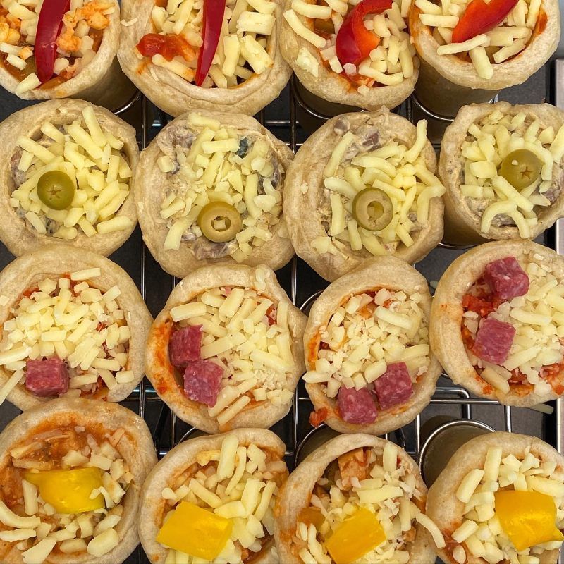 Een schaal met diverse kleine hartige taartjes, belegd met kaas, olijven, paprika en ham.