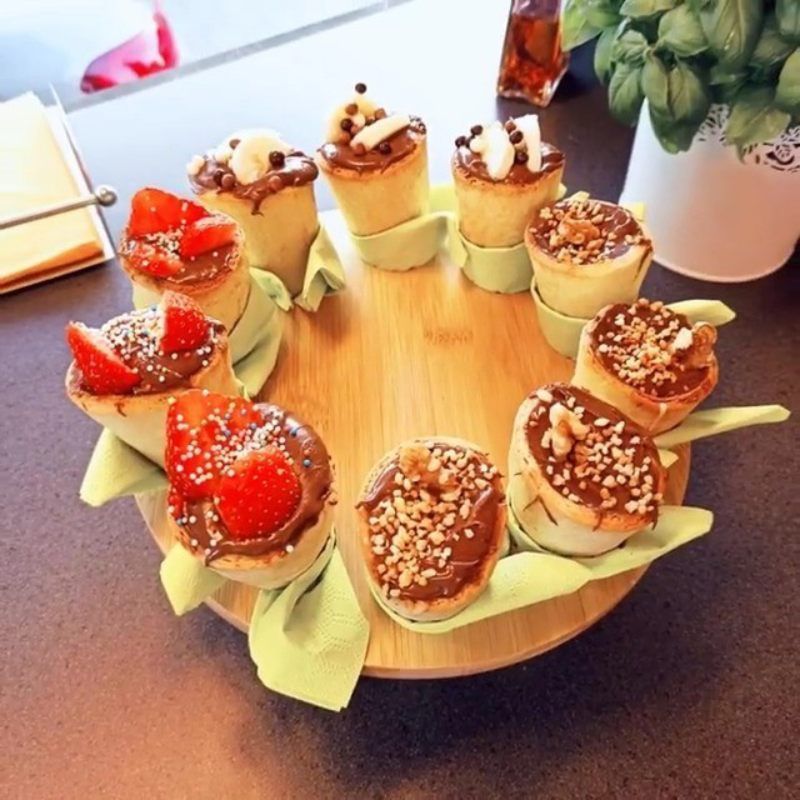 Dessertschotel met diverse mini-cupcakes, gegarneerd met aardbeien, chocolade en noten, op een houten dienblad.