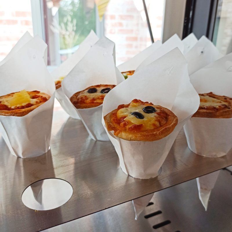 Mini-quiches in witte papieren bekertjes op een reflecterend dienblad bij een helder raam.