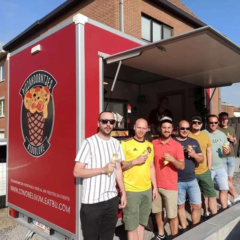 Mensen poseren naast een rode ijscowagen met een wafelhoornlogo.