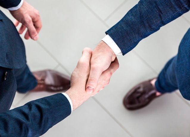 Dos personas de traje se dan la mano, vistas desde arriba, sobre un suelo de baldosas claras.