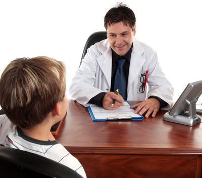 Un médico habla con un paciente al otro lado del escritorio en un consultorio médico, mientras escribe en un portapapeles.